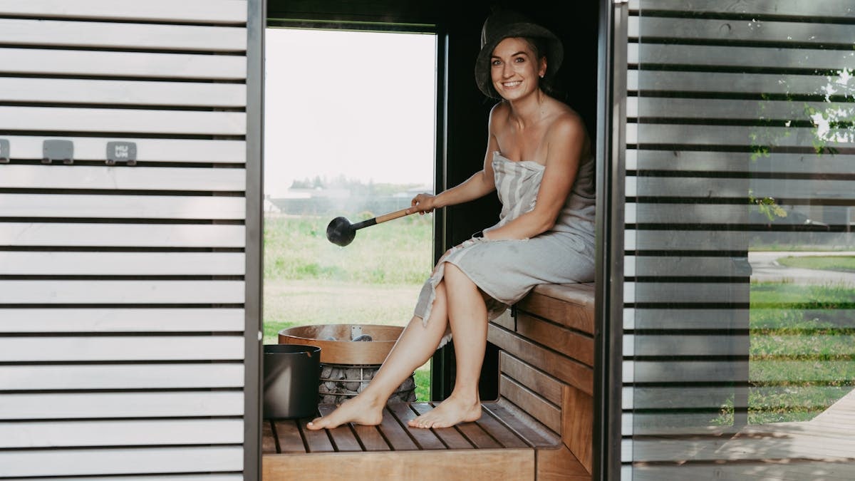 A woman in a sauna, wrapped in a towel, enjoying a relaxing steam session with a sauna hat.